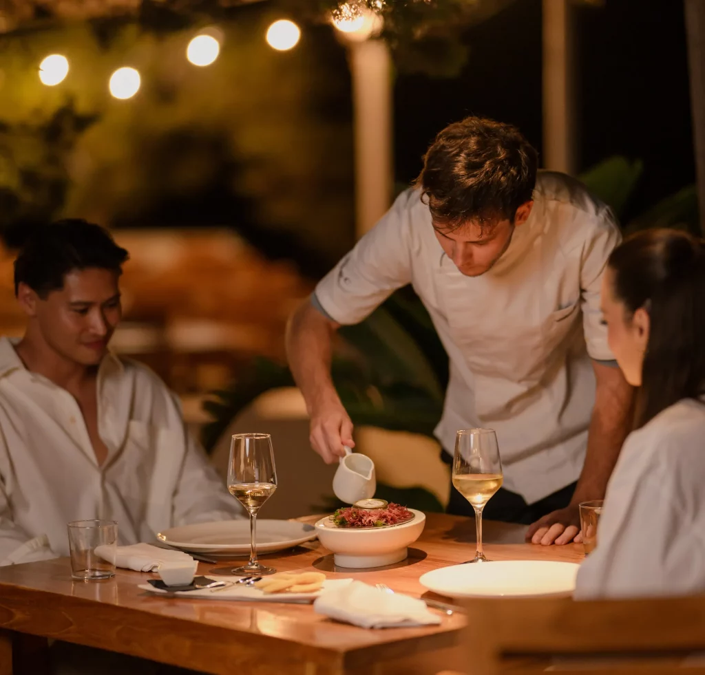 Un camarero sirviendo la cena a una pareja disfrutando en Cala Bassa Beach Club